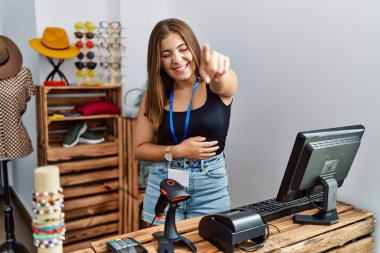 Perakende dükkanında açık mesajla pankart tutan genç esmer kadın sana gülüyor, eli vücudunun üzerinde kamerayı işaret ediyor, utanç ifadesi takınıyor. 