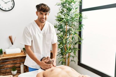 İki İspanyol erkek terapist ve hasta güzellik merkezinde yüz masajı yapıyorlar.