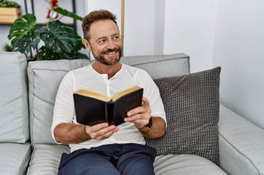 Middle age hispanic man smiling confident reading book at home