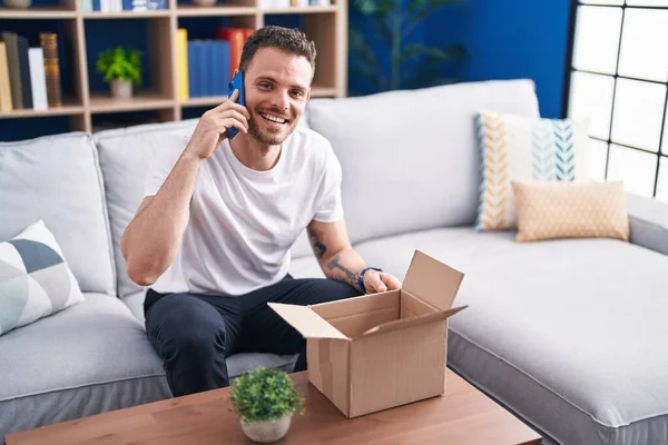 Genç İspanyol adam akıllı telefondan konuşuyor. Evde karton kutuları açıyor.