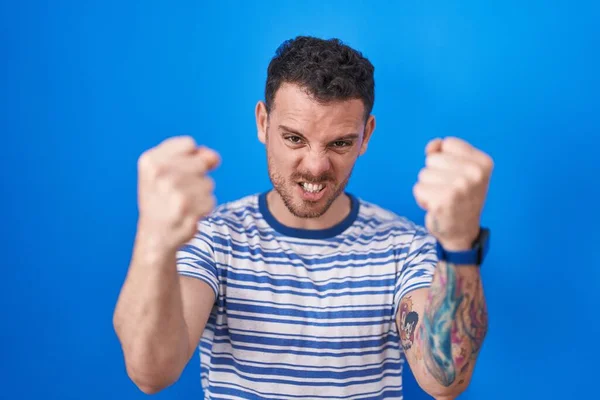 Homem Hispânico Jovem Sobre Fundo Azul Com Raiva Punhos Levantando — Fotografia de Stock