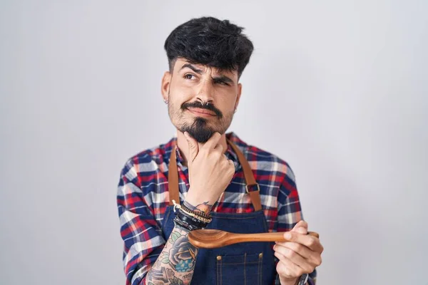 Young Hispanic Man Beard Wearing Apron Tasting Food Holding Wooden — Stockfoto