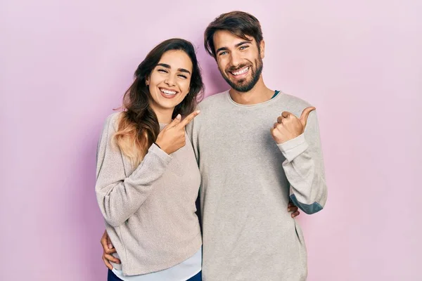 若いヒスパニック系のカップルが手と親指で後ろを指してカジュアルな服を着て 自信を笑顔 — ストック写真