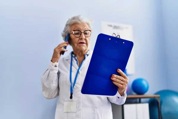 在理疗诊所 身穿理疗师制服的白发苍苍的老年妇女在智能手机上交谈 — 图库照片