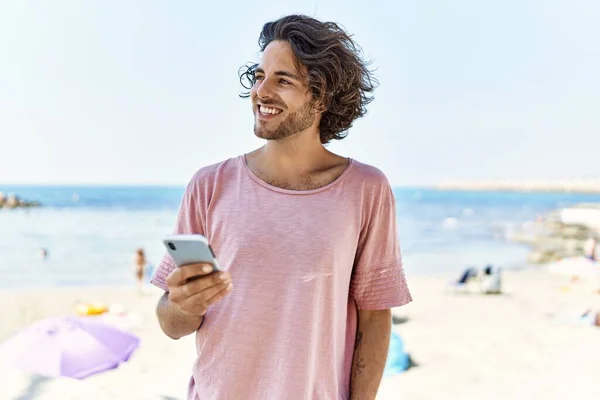 年轻的惊慌失措的男人在海滩用智能手机开心地微笑 — 图库照片