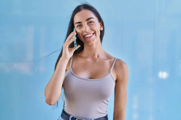 若いです美しいですヒスパニック女性笑顔自信を持って話して上のスマートフォン上で隔離された青の背景 — ストック写真