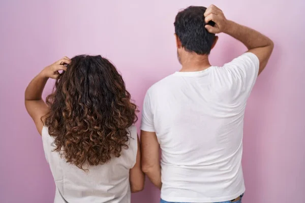 Middle age hispanic couple together over pink background backwards thinking about doubt with hand on head