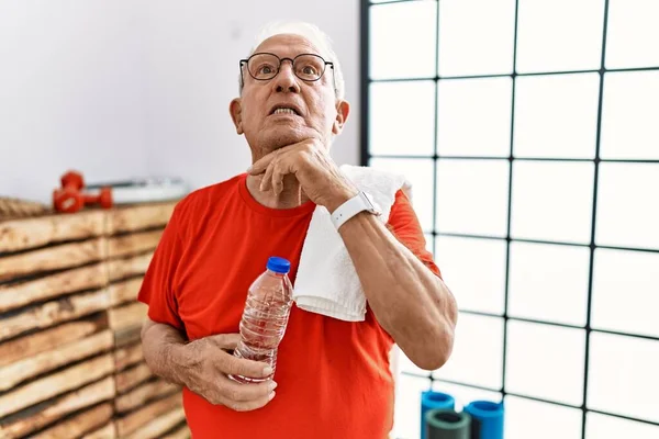 Senior man wearing sportswear and towel at the gym touching painful neck, sore throat for flu, clod and infection