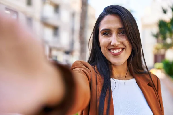 Young hispanic woman smiling confident making selfie by the camera at street