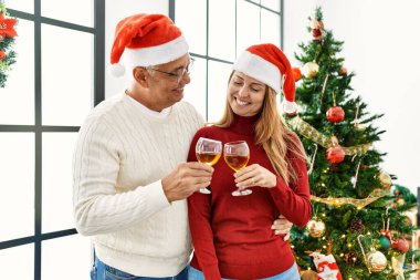 Orta yaşlı İspanyol çift mutlu bir şekilde gülümsüyor. Evde Noel ağacının yanında şampanya içiyorlar..