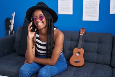Afrikalı Amerikalı kadın müzisyen gülümsüyor. Müzik stüdyosunda akıllı telefondan konuşuyor.