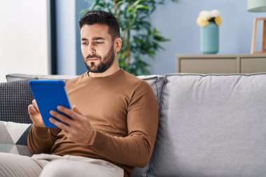 Genç İspanyol adam evdeki koltukta otururken dokunmatik ped kullanıyor.