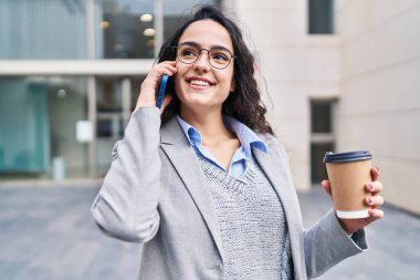 Genç İspanyol kadın yönetici kahve içiyor ve caddede akıllı telefondan konuşuyor.