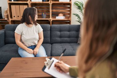 Down sendromlu İspanyol bir kız terapi yapıyor. Yüzünde gülümseme ve doğal ifadeyle yan yana bakıyor. Kendinden emin gülen. 