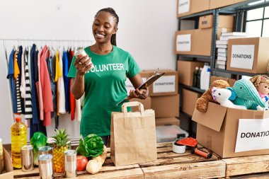 Genç Afro-Amerikalı gönüllü kadın yardım merkezinde içi yiyecek dolu kağıt torba hazırlıyor..