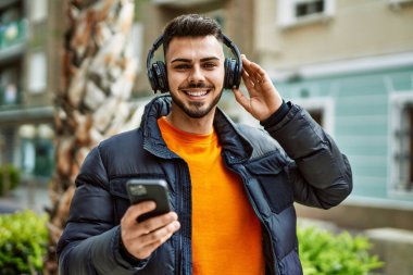 Yakışıklı, sakallı, neşeli, kendine güvenen, kışlık palto giyen, akıllı telefondan müzik dinleyen bir İspanyol.