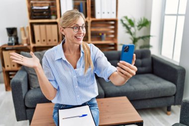 Beautiful woman doing online therapy session at consultation office celebrating achievement with happy smile and winner expression with raised hand 