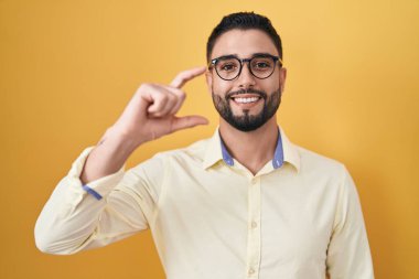 İspanyol genç adam iş kıyafetleri ve gözlük takıyor gülümsüyor ve el hareketleriyle hareket ediyor parmaklarıyla işaret yapıyor ve kameraya bakıyor. ölçüm kavramı. 