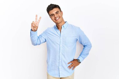 İzole edilmiş arka planda duran İspanyol gömlekli genç adam kameraya bakıp zafer işareti yapıyor. İki numara.. 