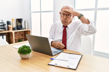 Senior man working at the office using computer laptop worried and stressed about a problem with hand on forehead, nervous and anxious for crisis 
