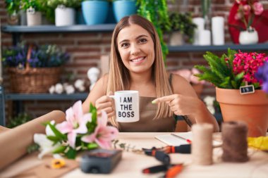 Young blonde woman working at florist shop holding i am the boss cup smiling happy pointing with hand and finger 