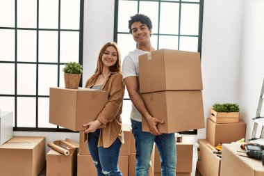 Genç çift yeni evinde karton kutu tutarken mutlu gülümsüyor.. 