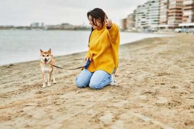 Kumsalda Shiba Inu köpeğiyle yürüyen güzel genç bir kadın.