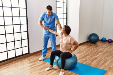 Latin erkek ve kadın fizyoterapist üniforması giyiyorlar rehabilitasyon merkezinde sağlıklı top kullanıyorlar.