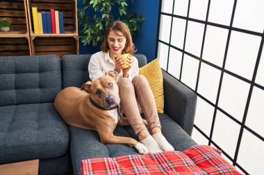 Kafkasyalı bir kadın kanepede köpeğiyle kahve içiyor.