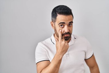 Young hispanic man with beard wearing casual clothes over white background pointing to the eye watching you gesture, suspicious expression 