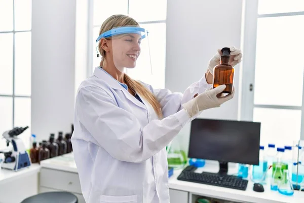 Jovem Loira Mulher Vestindo Cientista Uniforme Olhando Garrafa Laboratório — Fotografia de Stock