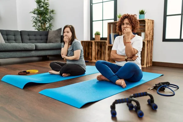 Family of mother and down syndrome daughter doing exercise at home looking stressed and nervous with hands on mouth biting nails. anxiety problem.