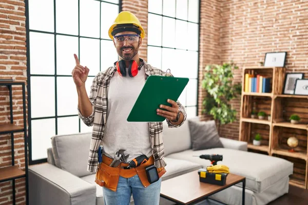 Sakallı, evde çalışan, gülümseyen, el ve parmağı kenarda gezen İspanyol bir adam. 