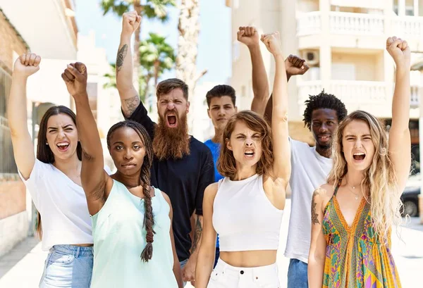 Group of young activists protesting with fists raised up standing at the city.