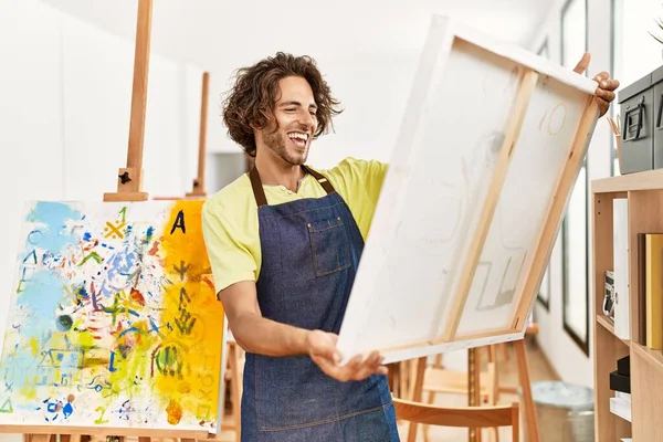 年轻的惊慌失措的艺术家在艺术工作室拿着画布开心地笑着 — 图库照片