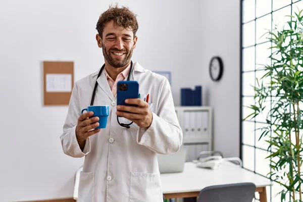 Jovem Hispânico Vestindo Uniforme Médico Usando Smartphone Beber Café Clínica — Fotografia de Stock