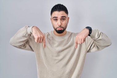 Genç yakışıklı adam izole edilmiş arka planda dikiliyor üzgün ve üzgün görünüyor, parmaklarıyla yön gösteriyor, mutsuz ve depresif.. 