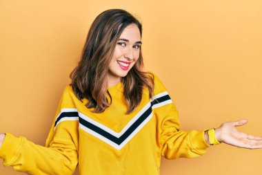 Gündelik kıyafetler giyen, gülümseyen, iki elini de açık gösteren, sunan ve reklamını yapan genç İspanyol kız. 