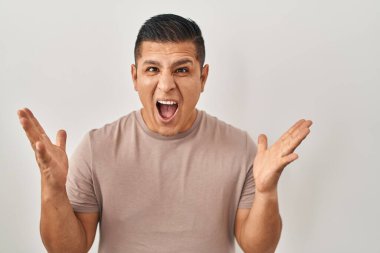 Hispanic young man standing over white background celebrating crazy and amazed for success with arms raised and open eyes screaming excited. winner concept 