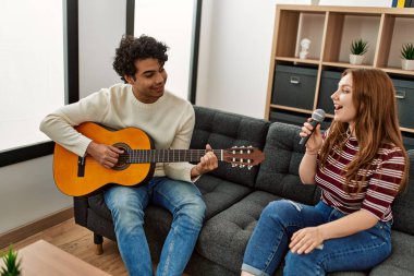 Genç çift klasik gitar çalıyor ve evde mikrofon kullanarak şarkı söylüyor..