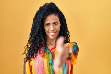 Orta yaşlı İspanyol bir kadın sarı arka planda durup dostça el sıkışarak selam ve hoş geldin diyor. başarılı iş. 