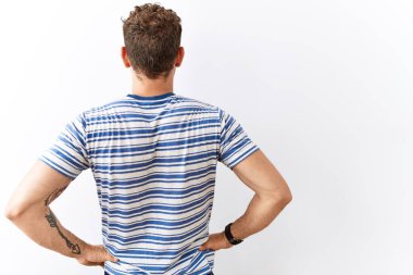 Yakışıklı genç adam izole edilmiş arka planda dikiliyor geriye bakıyor kollarını vücuduna dikiyor. 