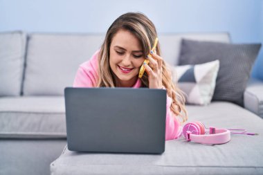 Young woman talking on smartphone lying on sofa at home