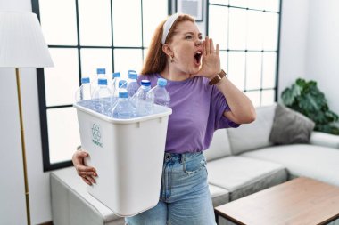 Genç kızıl saçlı kadın elinde plastik şişelerle çöpleri geri dönüşüm sepetini tutarak el ele bağırıyor ve çığlık çığlığa bağırıyordu. iletişim konsepti. 