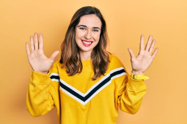 Genç İspanyol kız gündelik giysiler giyer ve parmaklarını on numara ile gösterir ve gösterirken kendinden emin ve mutlu bir şekilde gülümser.. 