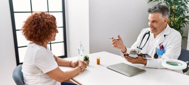 Doktor üniforması giyen orta yaşlı bir adam ve kadın klinikte tıbbi danışmanlık yapıyorlar.