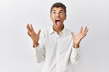 Genç, yakışıklı İspanyol adam izole edilmiş arka planda duruyor. Deli gibi bağırıyor, agresif bir ifadeyle bağırıyor ve kollarını kaldırıyor. hüsran kavramı. 