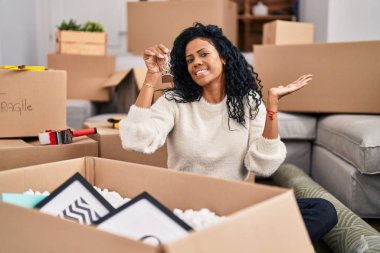 Orta yaşlı İspanyol kadın yeni evinin anahtarlarını tutuyor başarıyı mutlu bir gülümsemeyle kutluyor ve kazanan el kaldırarak ifade ediyor. 