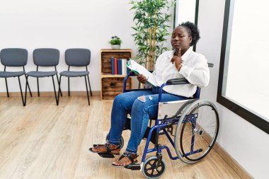 Bekleme odasında tekerlekli sandalyede oturan genç siyahi kadın parmakları çenesinde şüpheye odaklanmış ve yukarı bakıp merak ediyordu. 