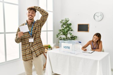 Young handsome man voting putting envelop in ballot box stressed and frustrated with hand on head, surprised and angry face 